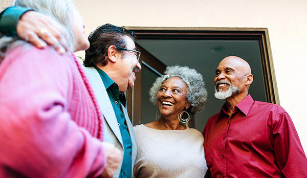 Four older adults smiling and talking together in a doorway.